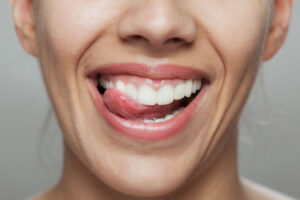 Close-up of a smiling woman licking her teeth, showing healthy white teeth and pink lips.